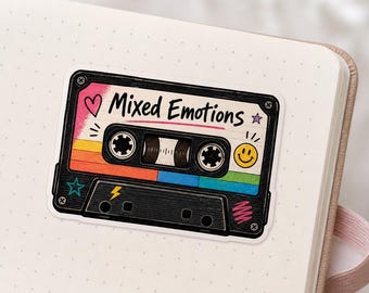 Könnte beinhalten: Ein Aufkleber in Form einer Kassette mit dem Schriftzug "Mixed Emotions". Das Design umfasst einen Regenbogenverlauf, ein Smiley, ein Herz und einen Stern. Der Aufkleber ist schwarz mit einem farbenfrohen Design.