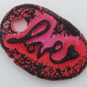 May include: A red and black ceramic ornament with the word "love" written in black script. The ornament has a hole at the top for hanging.