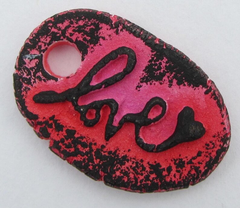 May include: A red and black ceramic ornament with the word "love" written in black script. The ornament has a hole at the top for hanging.