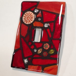May include: Red, orange, and black mosaic glass light switch cover with small white and red flowers and rhinestones.