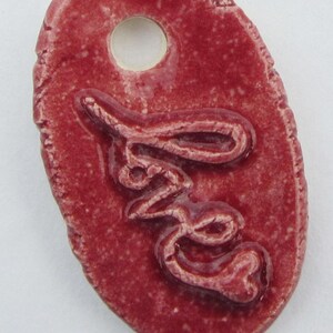 May include: A red ceramic tag with a hole for hanging. The tag has the word "Love" embossed on it.