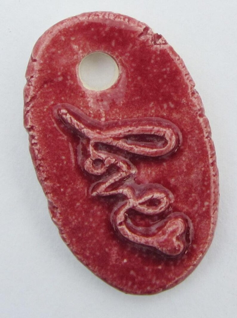 May include: A red ceramic tag with a hole for hanging. The tag has the word "Love" embossed on it.