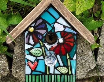 May include: A mosaic birdhouse with a wooden frame. The mosaic features a blue, green, and red floral design with a heart and a crystal embellishment.
