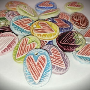 May include: A collection of ceramic heart-shaped ornaments in various colors, including red, blue, green, yellow, and purple. Each ornament features a white heart with a striped pattern.