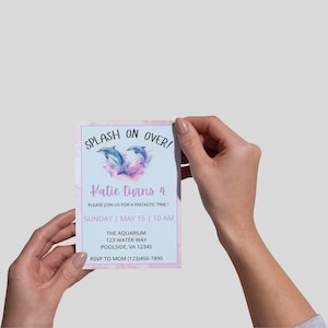 May include: A light blue invitation card with a pink border and watercolor accents. The card features two blue dolphins, the text "SPLASH ON OVER!" and "Katie turns 4". Additional text includes event details and RSVP information.