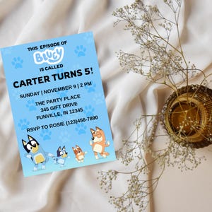 May include: A light blue invitation card with the text "CARTER TURNS 5!" and "BLUEY" branding. The card features cartoon dog characters and paw prints. The invitation includes party details: date, time, and location.