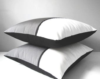 Funda decorativa de cojín Sunbrella para exteriores en gris y blanco con un moderno diseño de bloques de color y ribete negro. Cojines grises para sillas de patio y jardín.