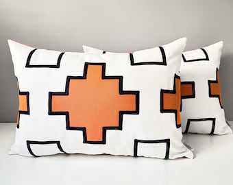 Duas capas de almofada Sunbrella pretas e brancas para exterior com detalhes em laranja, com design geométrico para decoração de piscina, pátio e jardim.