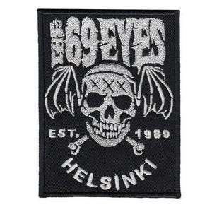 Könnte beinhalten: Schwarzer rechteckiger Aufnäher mit weißem Stickdesign. Das Design zeigt einen Totenkopf mit Fledermausflügeln, gekreuzten Knochen und dem Text "THE 69 EYES", "EST. 1989" und "HELSINKI".