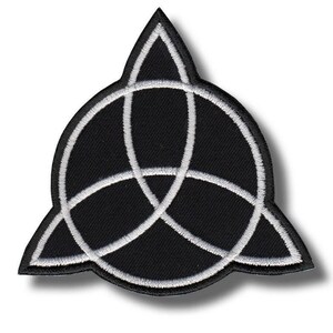 Può includere: Toppa ricamata in bianco e nero con un simbolo Triquetra. La toppa ha uno sfondo nero con un design bianco intrecciato. I bordi sono anch'essi delineati in bianco, creando un contrasto sorprendente. La toppa è probabilmente per abbigliamento o accessori.