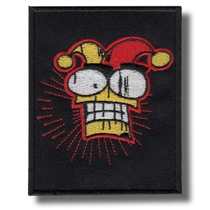 May include: A black embroidered patch featuring a cartoon jester face with a yellow head, white eyes, and a red and yellow jester hat. Red lines radiate from the jester's face. The patch is rectangular.