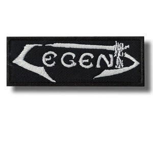 Może przedstawiać: Czarna prostokątna naszywka z białym haftem z napisem „LEGEND”. Słowo znajduje się wewnątrz białego strzałkowatego wzoru. Naszywka ma cień.