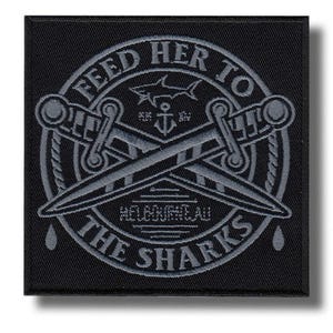 Pode incluir: Um patch quadrado preto com um design cinza. O design apresenta espadas cruzadas, um tubarão, uma âncora e o texto "FEED HER TO THE SHARKS" em um padrão circular. O texto "MELBOURNE AU" também está presente.