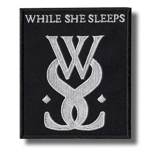 Könnte beinhalten: Schwarzer quadratischer Aufnäher mit weiß gesticktem Text und Design. Der Text "WHILE SHE SLEEPS" steht oben. Darunter befindet sich ein stilisiertes "W" über einem "S"-Design. Zwei kleine Rauten befinden sich auf beiden Seiten des "S".