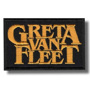 May include: A rectangular black patch with the embroidered text "GRETA VAN FLEET" in gold. The patch has a black border and a slight shadow effect, suggesting a raised design. The lettering is in a stylized, vintage font.