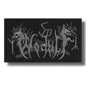 May include: Black rectangular patch with grey embroidered text, likely a band logo. The patch has a black border and is probably made of fabric. The design is intricate and detailed, with a gothic aesthetic.