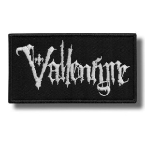 Op de afbeelding: Zwart rechthoekig embleem met de witte tekst "Vallenfyre" in een gotisch lettertype. Het embleem heeft een zwarte rand en is waarschijnlijk gemaakt van stof. De tekst is gestileerd en lijkt geborduurd.