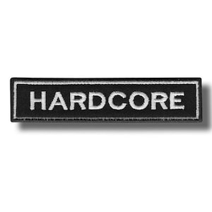 Peut inclure: Écusson rectangulaire noir avec le mot "HARDCORE" brodé en lettres majuscules blanches. L'écusson a une bordure blanche et est posé sur un fond blanc.