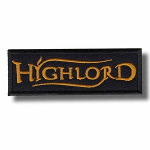 May include: Black rectangular embroidered patch featuring the gold text "HIGH LORD". The lettering is in a decorative font with a curved underline. The patch has a black border and is designed for application on fabric items.