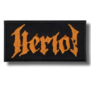 May include: Black rectangular patch with the word "Herod" embroidered in orange gothic lettering. The patch has a black border and is likely designed to be sewn or ironed onto clothing or accessories.