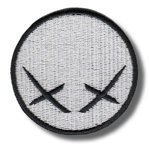 Könnte beinhalten: Runder, gestickter Aufnäher mit weißem Hintergrund und zwei schwarzen 'X'-Formen, die Augen darstellen. Der Aufnäher hat einen schwarzen Rand. Ideal zum Anpassen von Kleidung oder Accessoires.