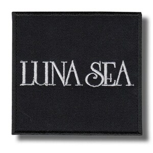 Może przedstawiać: Czarna kwadratowa naszywka z haftowanym białym napisem "LUNA SEA". Naszywka ma teksturowany wygląd i szytą obwódkę. Projekt jest prosty, a tekst jest w kroju szeryfowym.