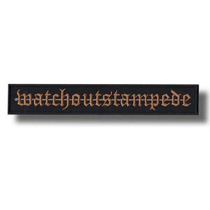 May include: A black rectangular patch featuring the embroidered words "watchoutstampede" in a gothic font, using a gold-brown thread. The patch has a simple, minimalist design.