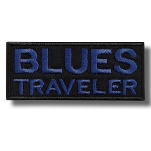 Könnte beinhalten: Ein rechteckiger, schwarzer Aufnäher mit den Worten "BLUES TRAVELER" in blauer Stickerei. Der Text ist fett und ohne Serifen, und der Aufnäher hat einen genähten Rand.