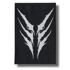 以下が含まれることがあります： 黒い長方形のパッチ。白で様式化されたオオカミまたは生き物の顔のデザイン。デザインは、シャープで角張った線と対称的な配置が特徴です。パッチはおそらく布製で、衣類やアクセサリーに縫い付けたり、アイロンをかけたりするのに適しています。