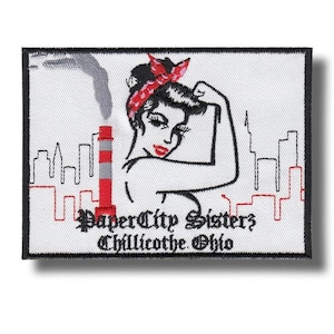Peut inclure: Écusson brodé représentant une femme stylisée fléchissant son bras, portant un bandana rouge et du rouge à lèvres. Le motif comprend une cheminée d'usine, une ligne d'horizon et le texte "Paper City Sisters Chillicothe, Ohio."