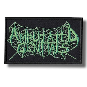 May include: A rectangular black patch with the words "AMPUTATED GENITALS" embroidered in green, stylized with a web-like design. The patch is likely for clothing or accessories.