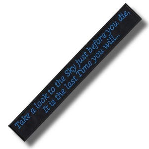 Puede incluir: Parche rectangular negro con texto bordado en azul: "Take a look to the Sky just before you die, It is the last Time you will..." El parche está en ángulo, con fondo blanco.