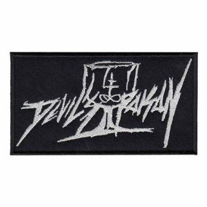May include: Black rectangular patch with white embroidered text that reads "DEVIL'S BAZAAR" in a stylized font. The patch features a symbol above the text. The patch is likely for clothing or accessories.