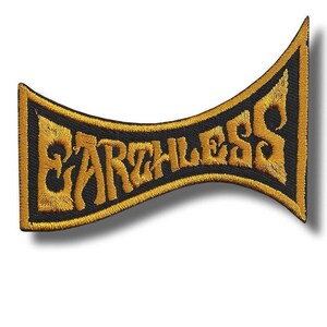 Puede incluir: Parche bordado con la palabra "EARTHLESS" en hilo dorado sobre fondo negro. El parche tiene una forma curva única con un borde dorado. El diseño es llamativo, adecuado para chaquetas, bolsos u otras prendas.