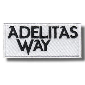 May include: A rectangular white patch with black embroidered text that reads "ADELITAS WAY". The patch has a white border and a textured surface. The text is in a bold, sans-serif font.