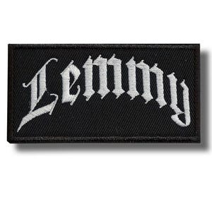 Może przedstawiać: Czarna prostokątna naszywka z napisem "Lemmy" wyszytym na biało gotycką czcionką. Naszywka jest przeznaczona do przyszywania do odzieży lub akcesoriów i ma czarną obwódkę.