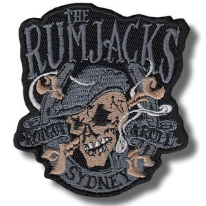 Op de afbeelding: Geborduurde patch met een schedel met een piratenhoed, gekruiste zwaarden en de tekst "THE RUMJACKS SYDNEY". De patch is voornamelijk zwart, met grijze, bruine en witte details. Het ontwerp heeft een vintage uitstraling.