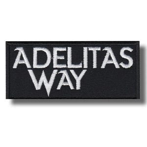 Può includere: Toppa rettangolare nera con testo ricamato bianco "ADELITAS WAY". Il design è pulito e minimalista, con il testo centrato sullo sfondo nero. Il carattere è in grassetto, in stile sans-serif.
