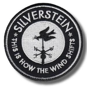 May include: Circular black and white embroidered patch with the text "SILVERSTEIN" at the top and "THIS IS HOW THE WIND SHIFTS" around the edge. The center features a weather vane design.
