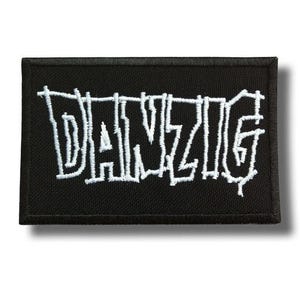 May include: Black rectangular patch with the white embroidered word "DANZIG". The patch has a black border and a white embroidered font. The patch is likely for clothing or accessories.