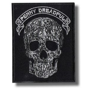 May include: Black rectangular patch with a white embroidered skull design. The skull is intricately patterned with various shapes and figures. Above the skull, a white banner reads "PENNY DREADFUL". The patch has a black border.