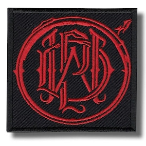 May include: Square black patch with a red embroidered design. The design features intertwined letters within a circular frame, with decorative flourishes. The patch has a textured appearance and a clean, crisp border.