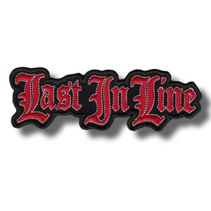 Puede incluir: Parche bordado negro con la frase "Last In Line" en fuente gótica. El texto es rojo con contorno blanco, sobre un fondo negro. El parche tiene un borde negro.
