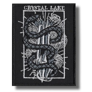 May include: Black embroidered patch with the text "CRYSTAL LAKE" at the top. The patch features a detailed design of a snake coiled around a central structure, with intricate white and grey stitching.