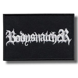 May include: Black rectangular patch with the white embroidered text "Bodysnatcher" in a gothic font. The patch has a black border and is likely for clothing or accessories.