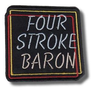 Può includere: Una toppa quadrata nera ricamata con le parole "FOUR STROKE BARON" in filo bianco, azzurro e beige. La toppa ha un bordo rosso e giallo.