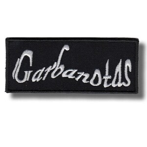 May include: A black rectangular patch featuring the word "Garbanotas" in white cursive embroidery. The patch has a black border and a shadow effect.