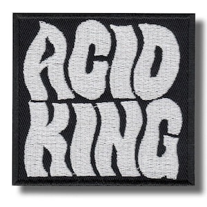 May include: Embroidered patch with the words "ACID KING" in white, stylized, wavy lettering on a black square background. The patch has a textured appearance, suggesting it is made of fabric or a similar material. The design is bold and eye-catching.