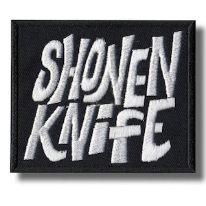 Könnte beinhalten: Schwarzer rechteckiger Aufnäher mit weiß gesticktem Text "SHONEN KNIFE". Der Aufnäher hat einen schwarzen Rand und einen Schatteneffekt.