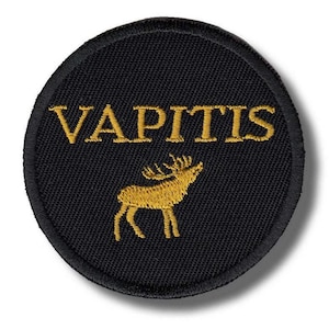 May include: A circular black patch featuring the word "VAPITIS" in gold, above a gold deer silhouette. The patch has a black border. Likely an emblem or patch for clothing or accessories.